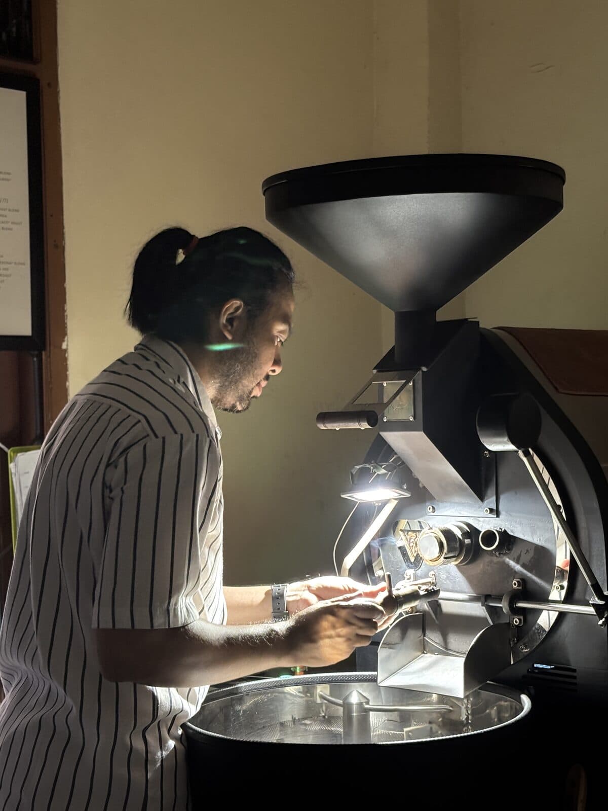 Operator memeriksa biji kopi yang keluar dari mesin sangrai